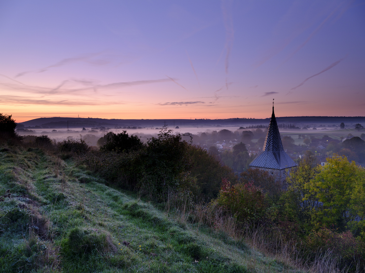 Early morning autumnal mist over East Meon village with Butser Hill and the South Downs in the background, South Downs National Park, Hampshire, UK