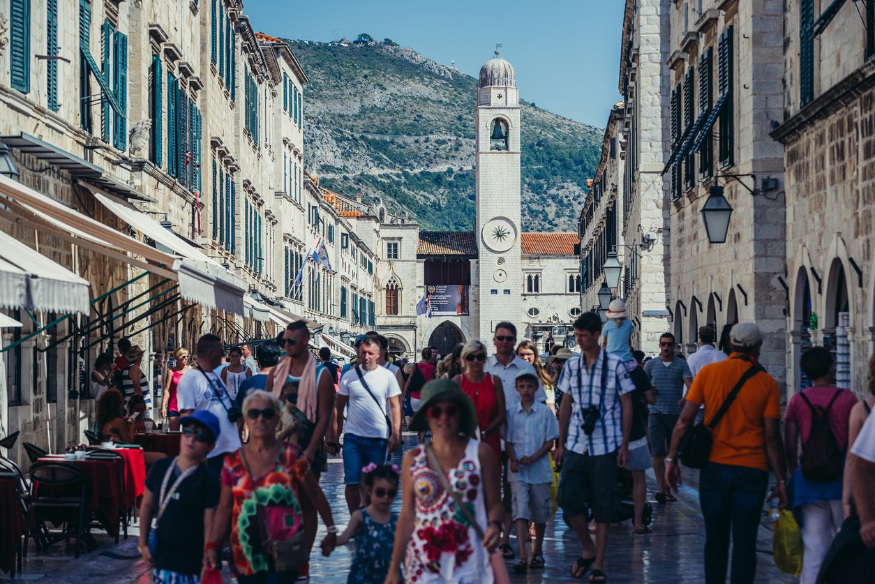 Tourists walk on main street of Old Town in Dubrovnik called Stradun, with Bell Tower on the background.