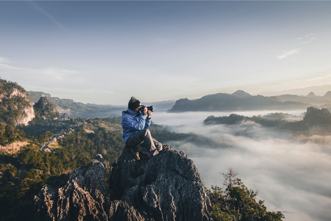 A hiker on top of a mountain crag, photographing cloud-shrouded mountains.