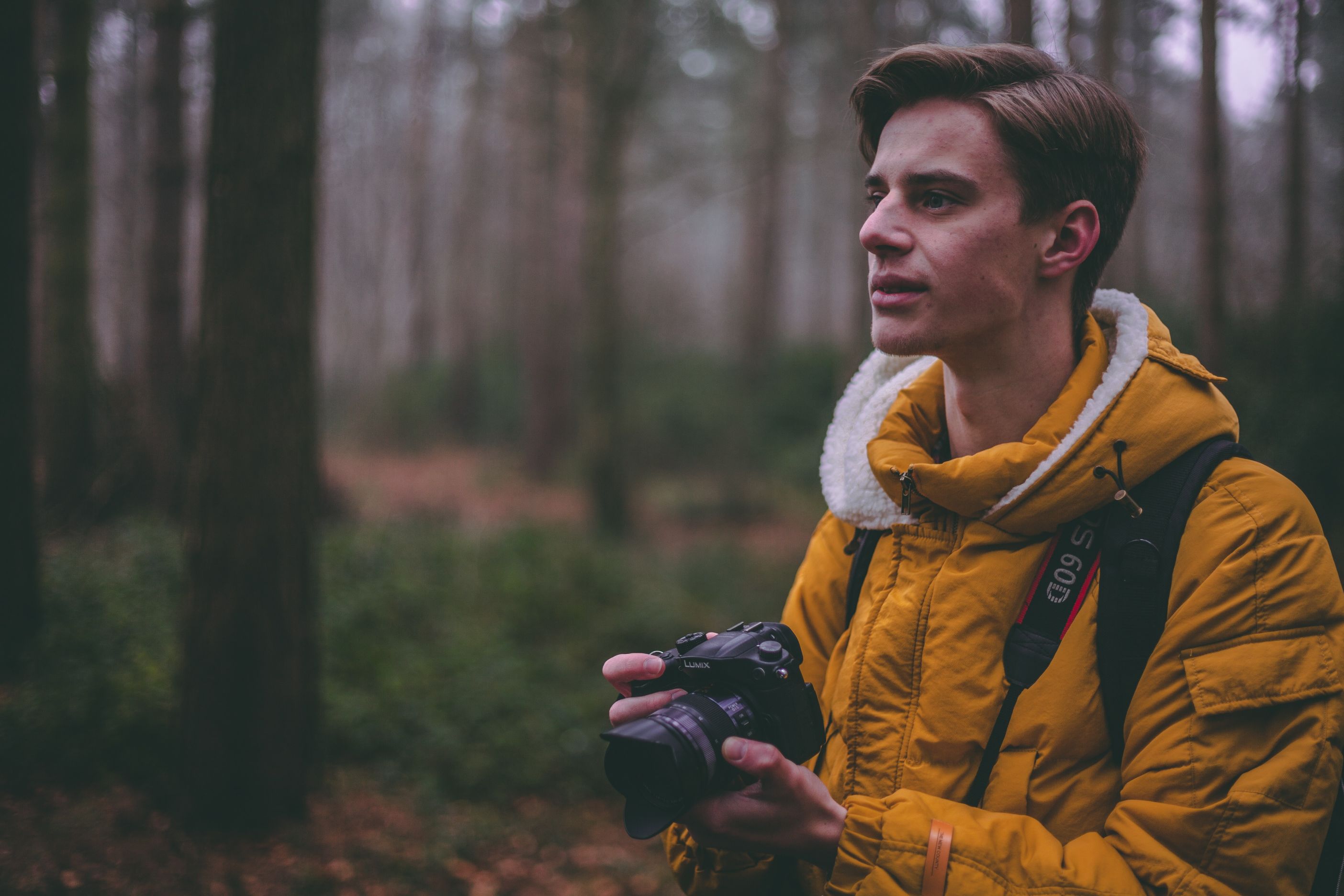 A man stands in a woodland holding a camera.