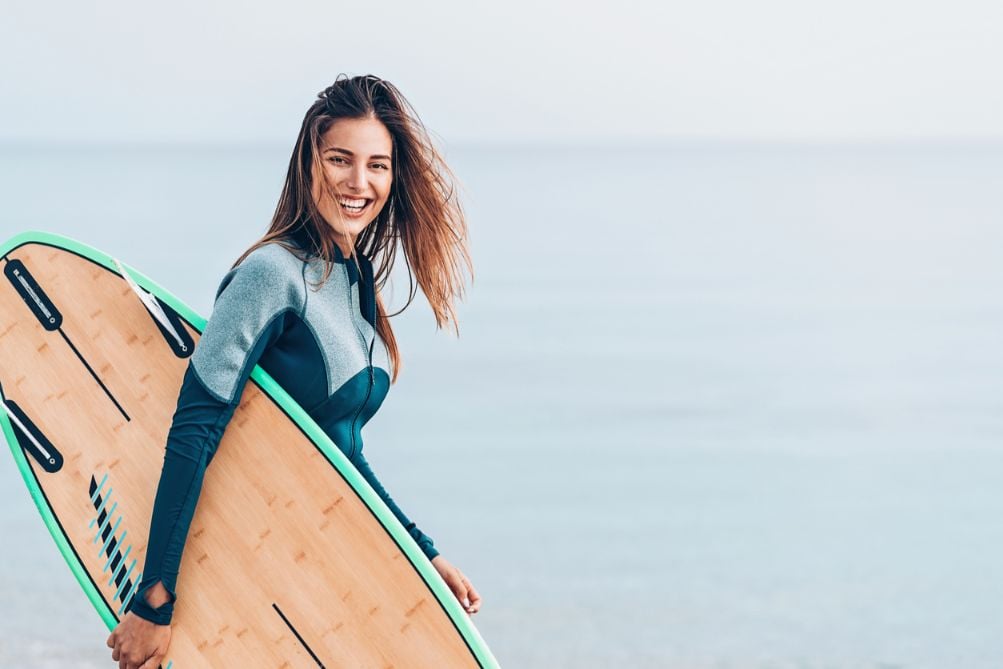 A smiling woman surfer holding her surfboard.