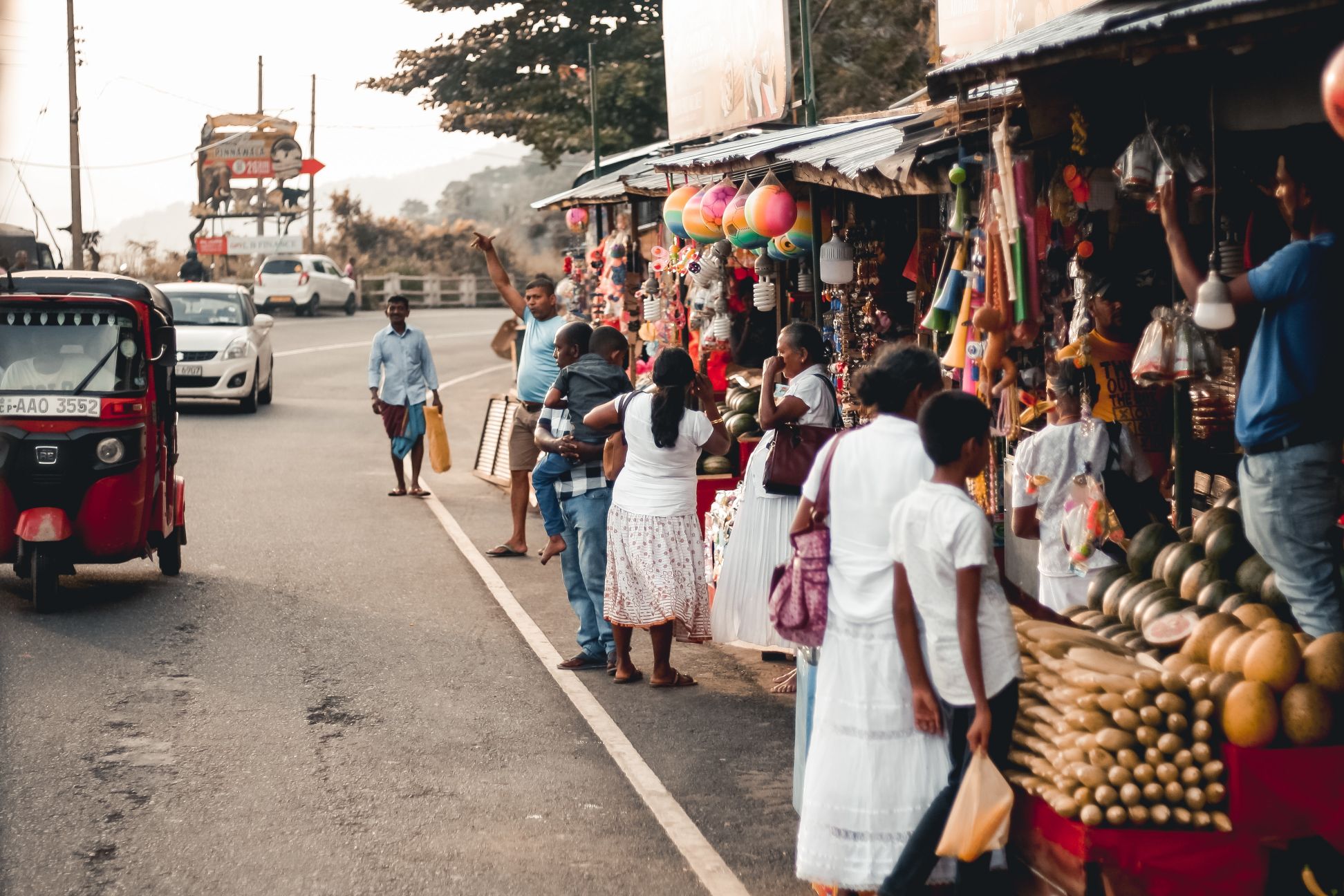A roadside in Sri Lanka, with people waiting for taxis and browsing stalls.