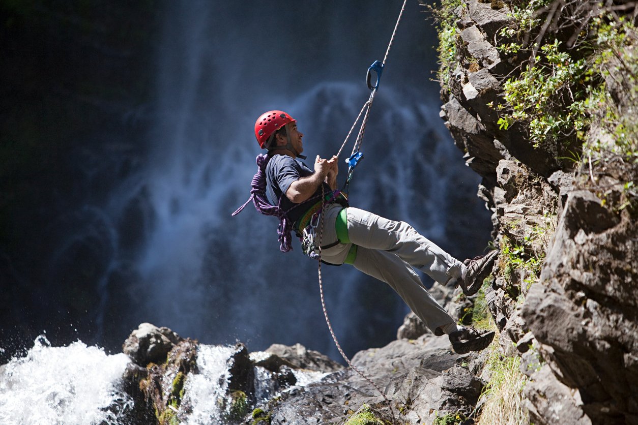 A man abseiling near a waterfall.