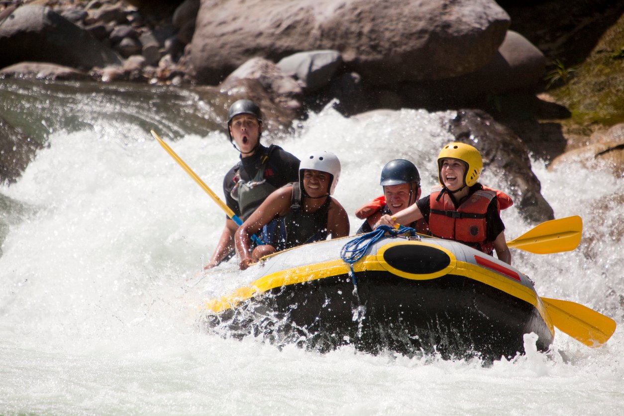 A white water rafting group on a rapid, wearing full protective gear.