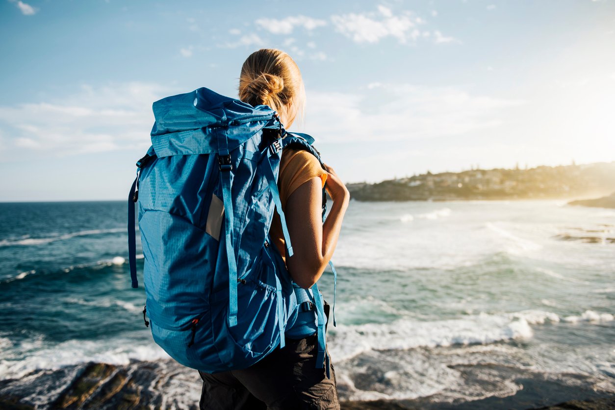 A female hiker wearing a backpack and looking out over the ocean.