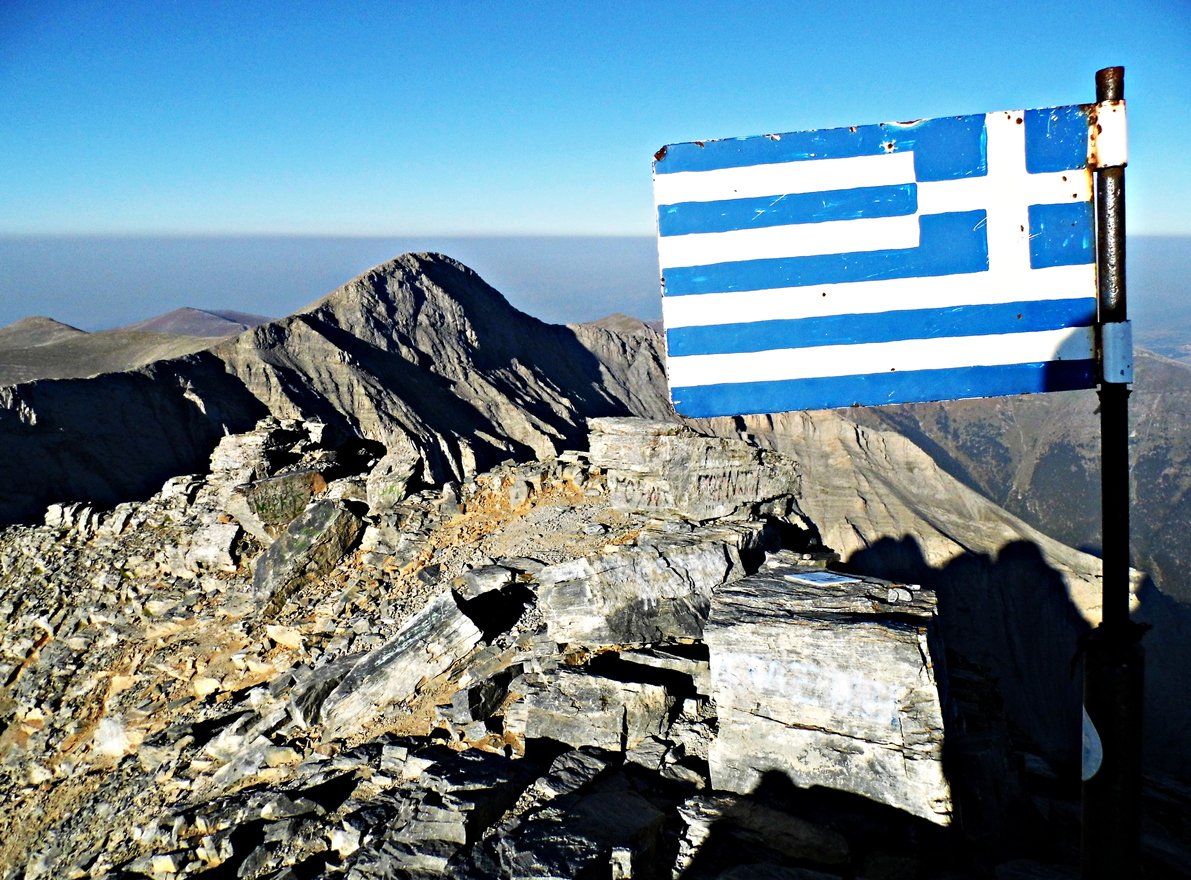 The Greek flag and Skolio Peak behind, as seen from the summit of Mount Olympus