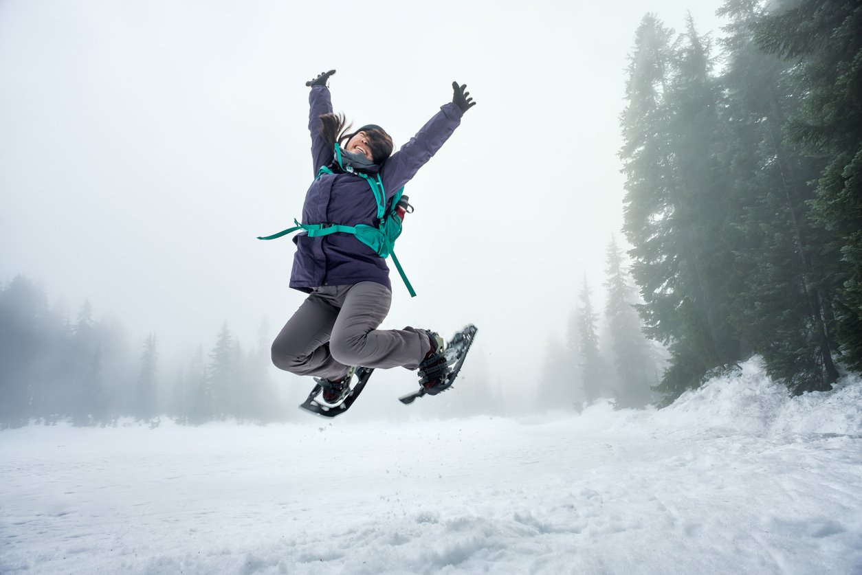 A woman jumping in the air wearing snowshoes.