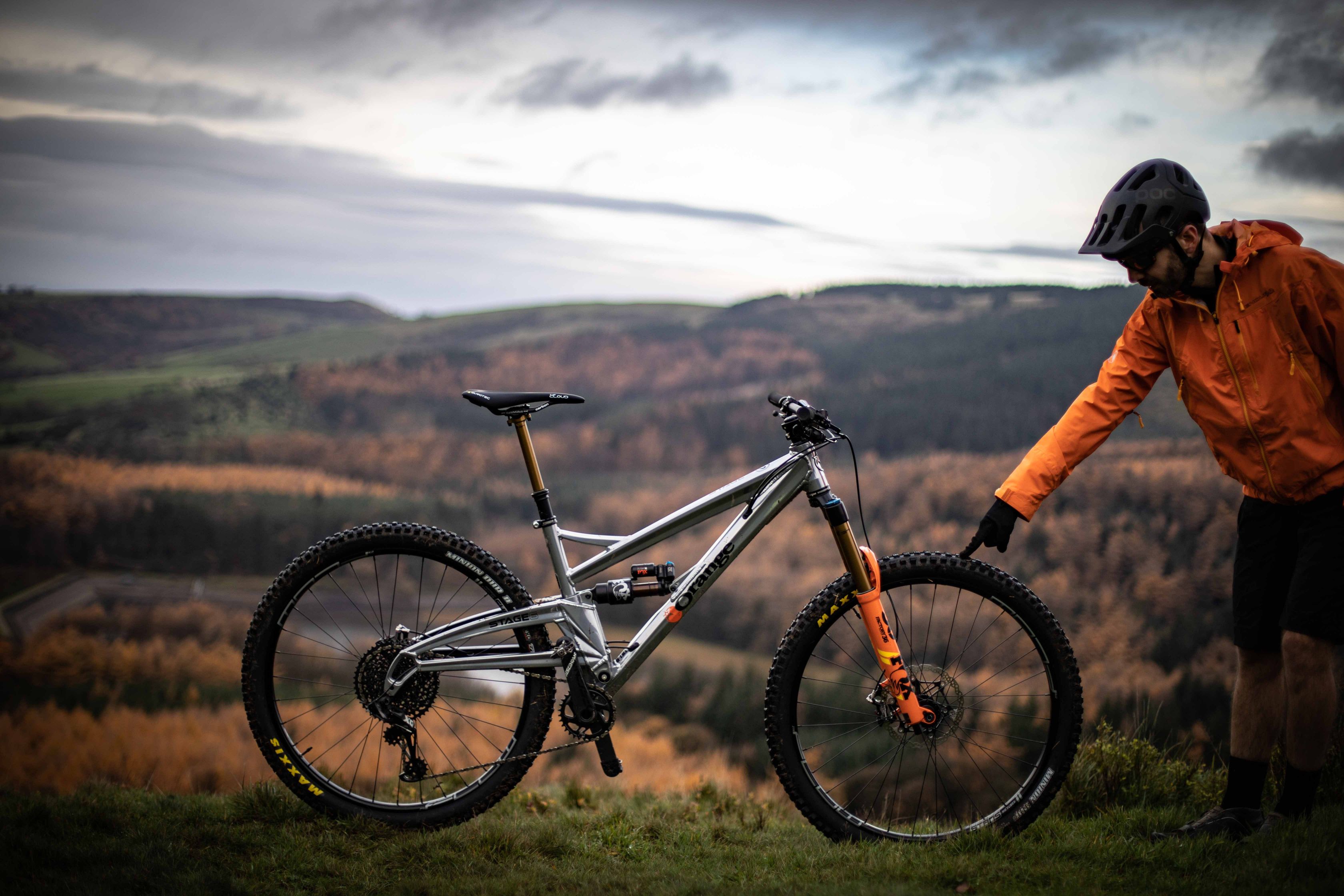 A cyclist points to his mountain bike - there is a backdrop of hills behind