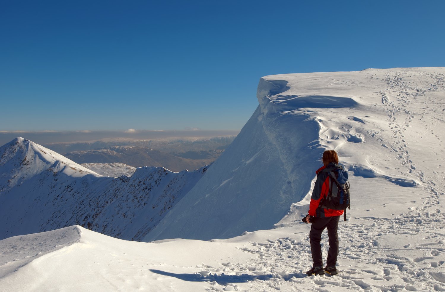 A hiker looking out at the snow covered peaks of Helvellyn