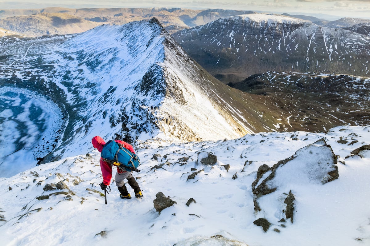 A hiker descending Helvellyn towards Striding Edge in the snow