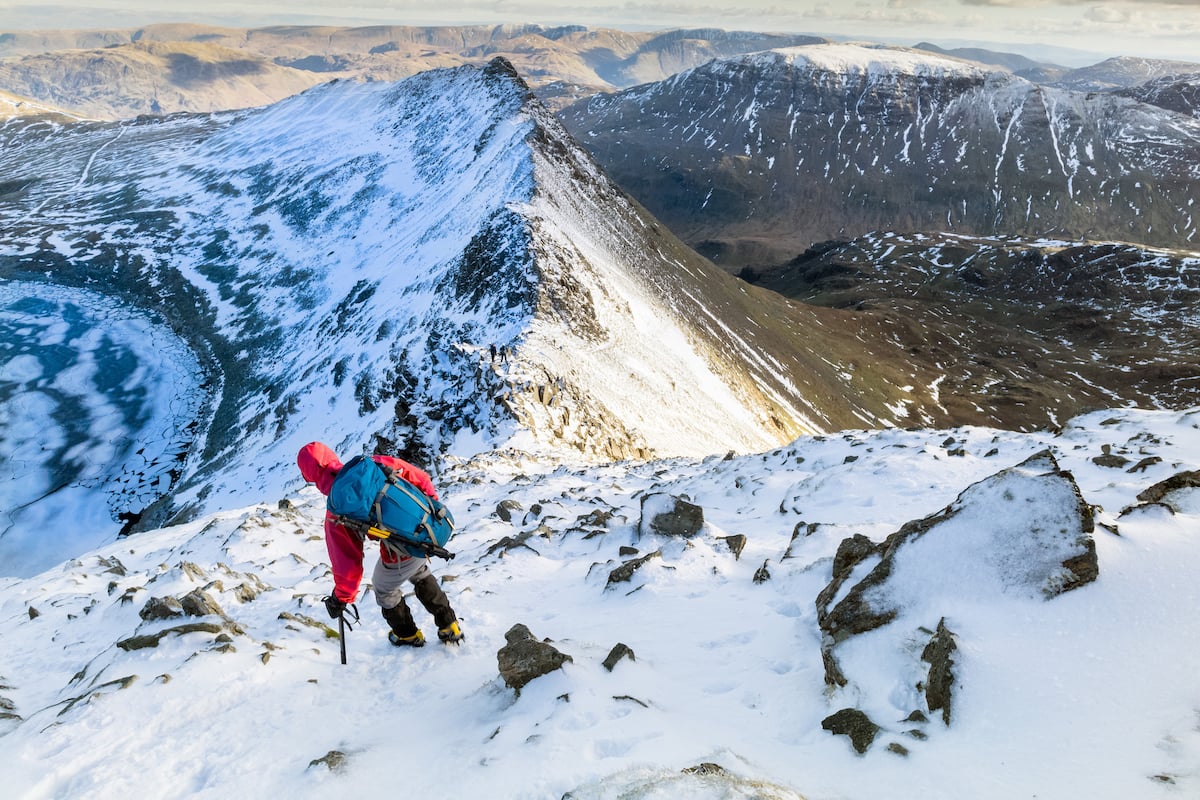 A hiker descending Helvellyn towards Striding Edge in the snow