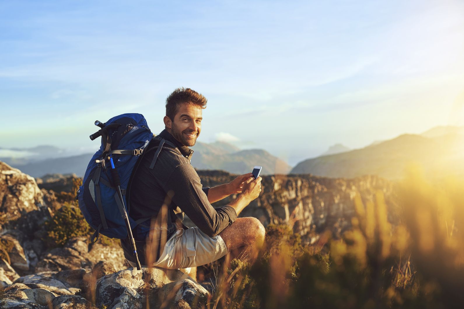 A solo male hiker in the mountains, holding a phone.