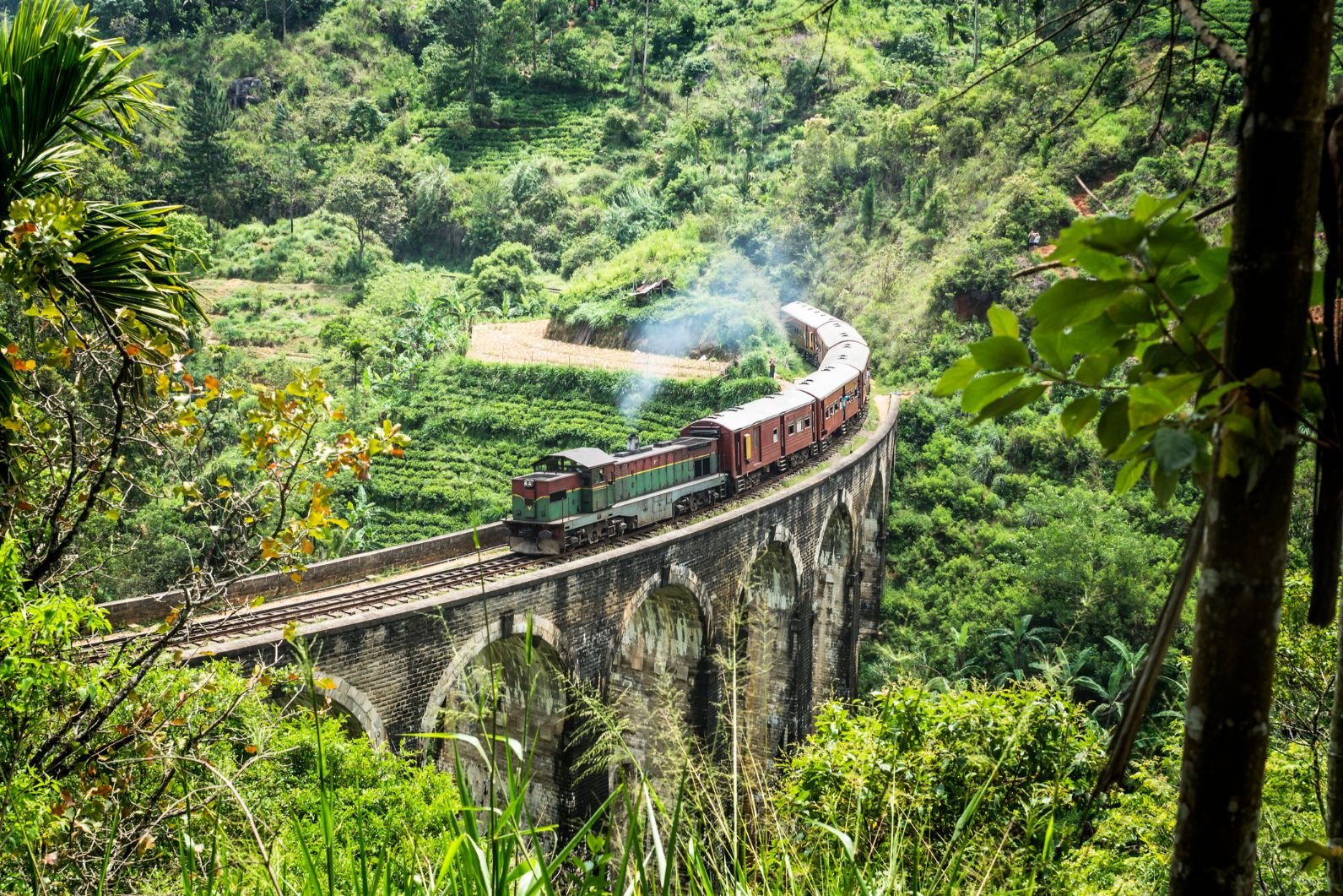 A steam train rolls around a viaduct amongst the lush greenery of Sri Lanka.