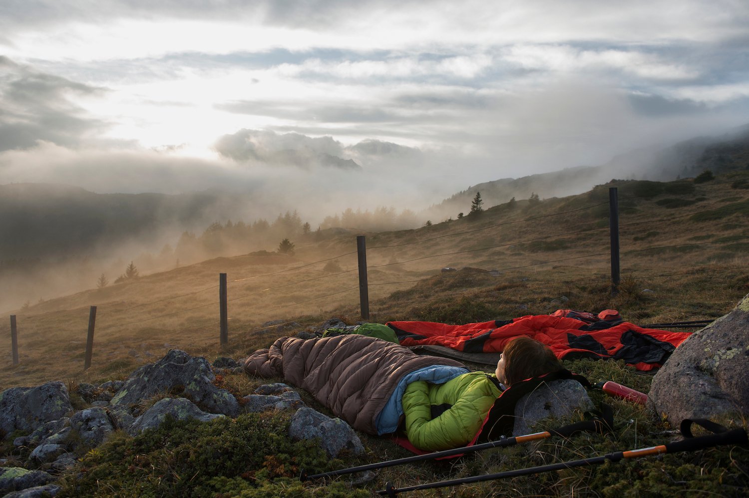 A woman is sleeping in a sleeping bag, looking out on a misty hill