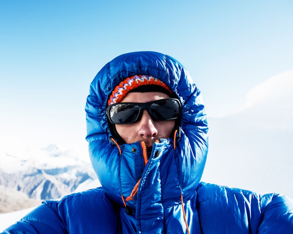 A man in a puffy blue jacket in front of mountains