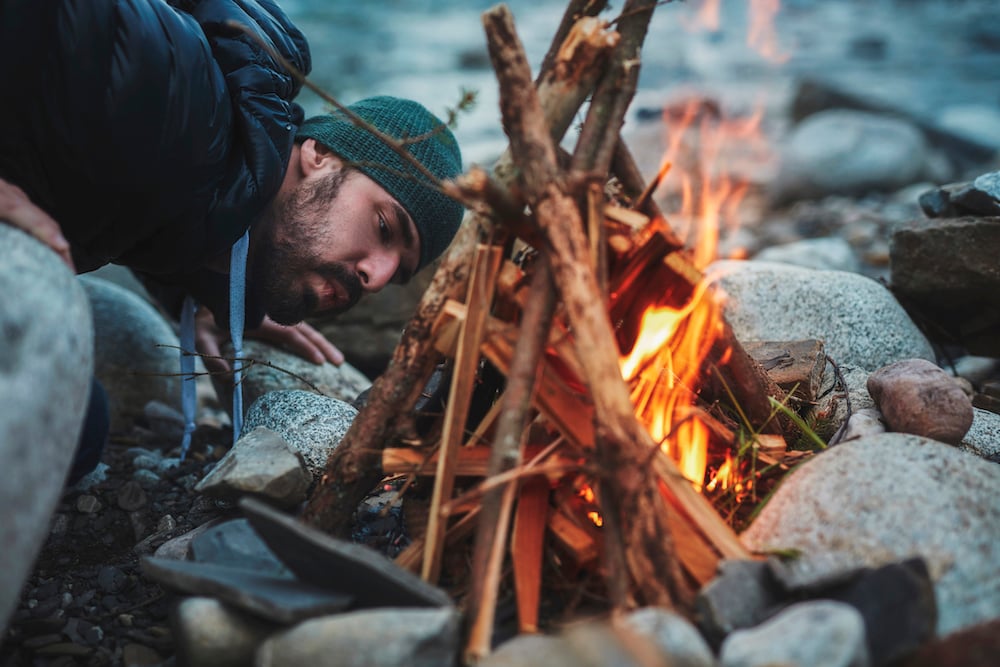 A man blowing into the campfire to help get it going