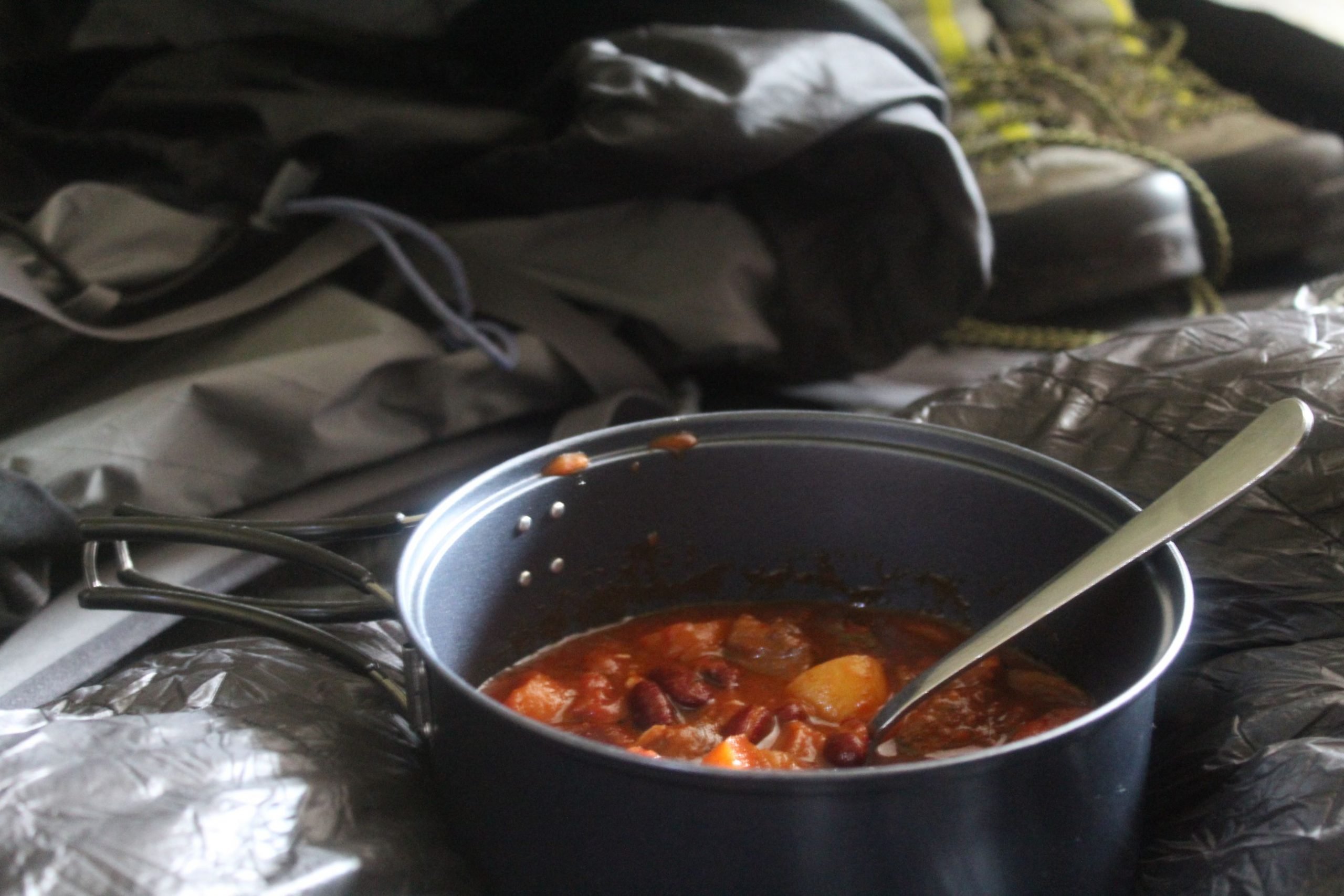 A pot of campfire stew on a tarpaulin