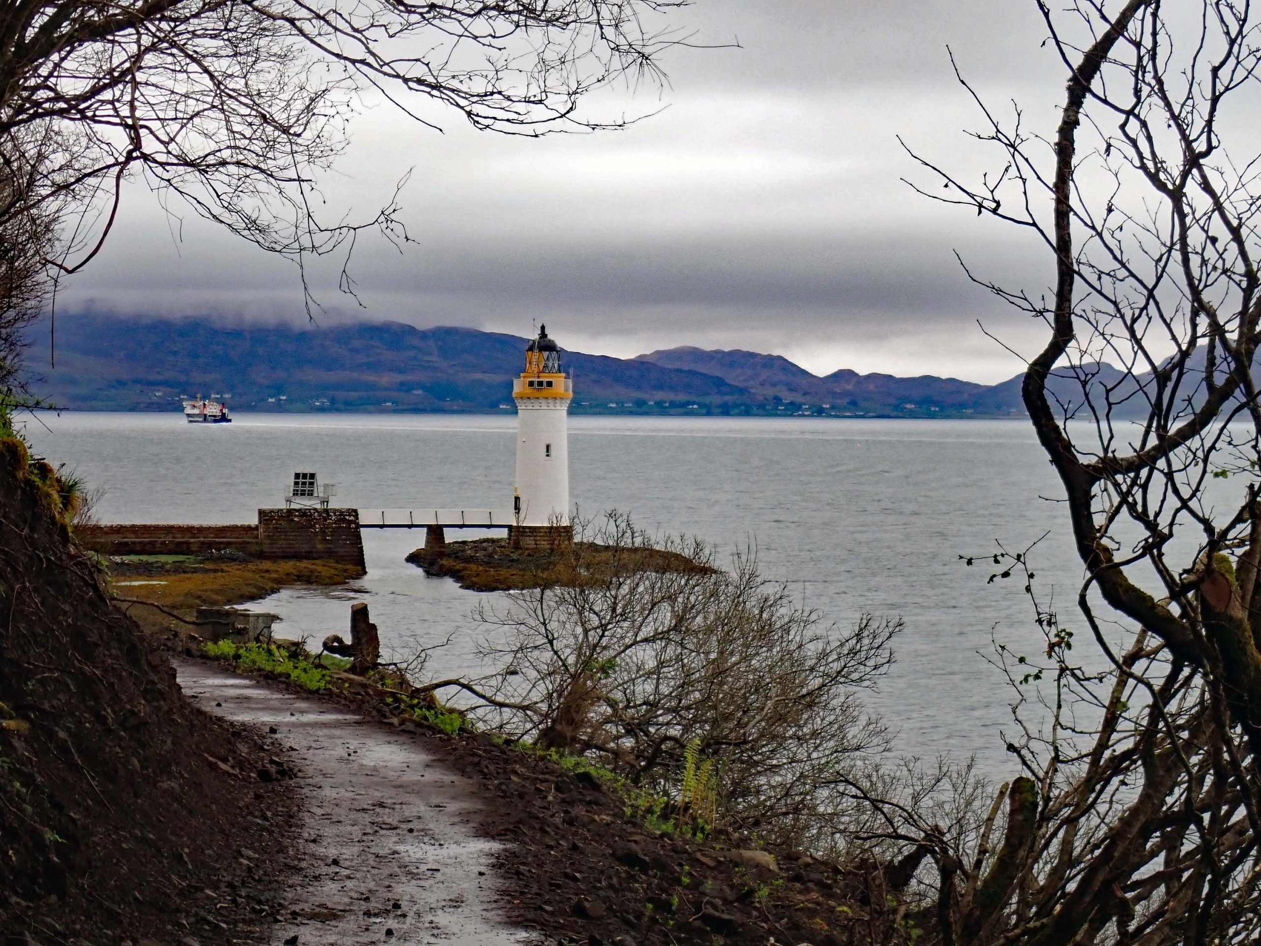 A hiking trail to a lighthouse, with sea and mountains in the background.