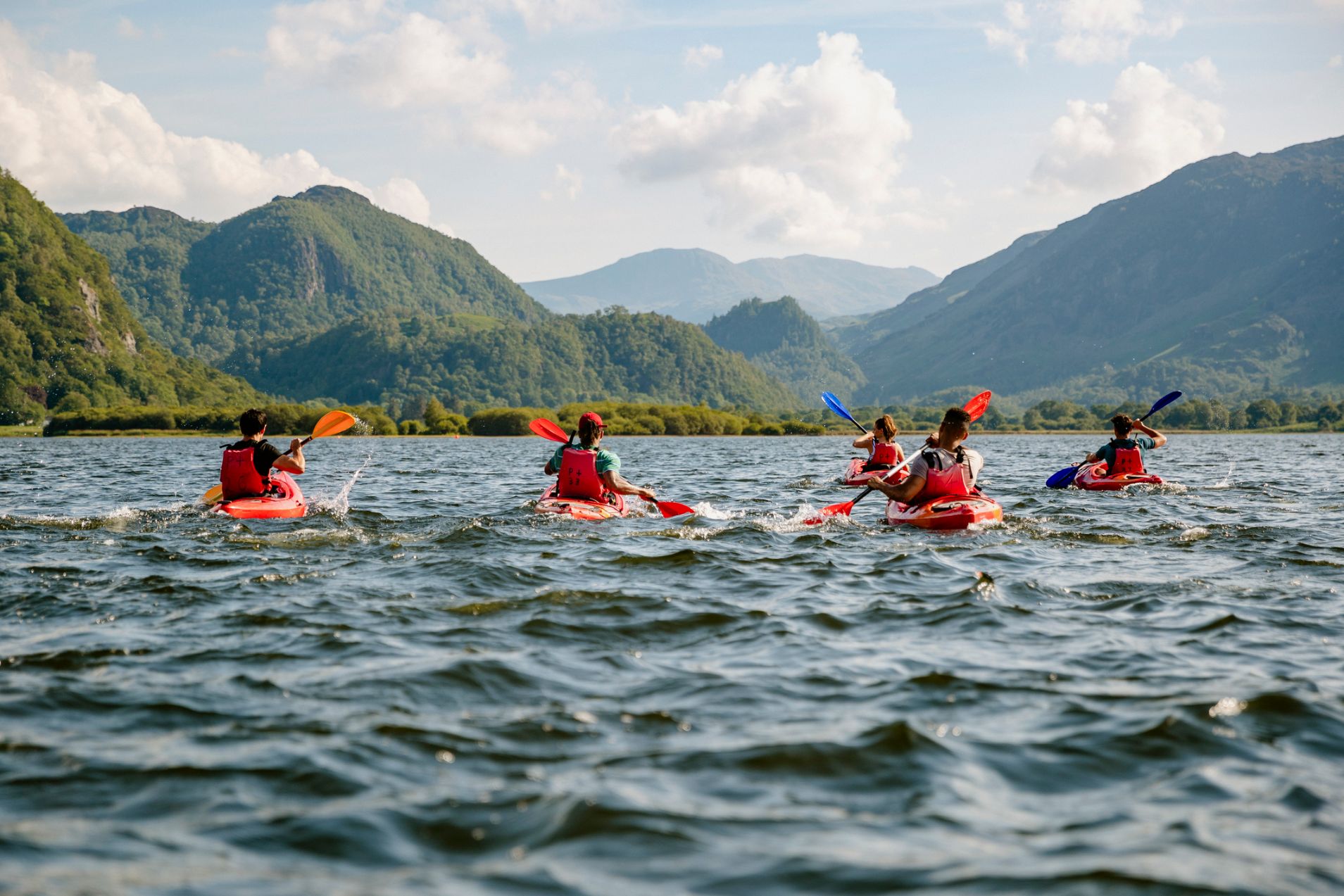 Five kayakers head out to paddle in a scenic location, surrounded by mountains.
