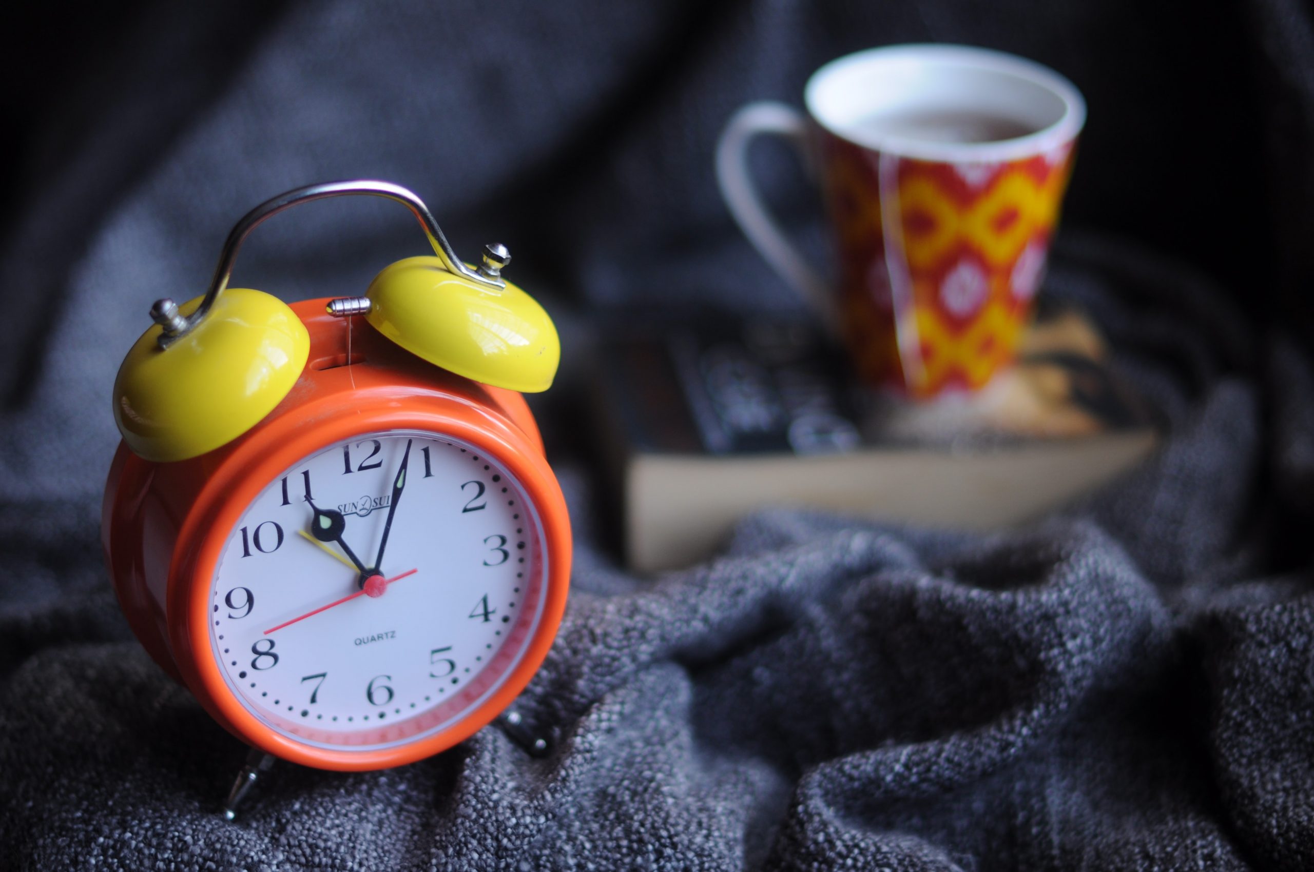 An alarm clock with a coffee cup in the background.