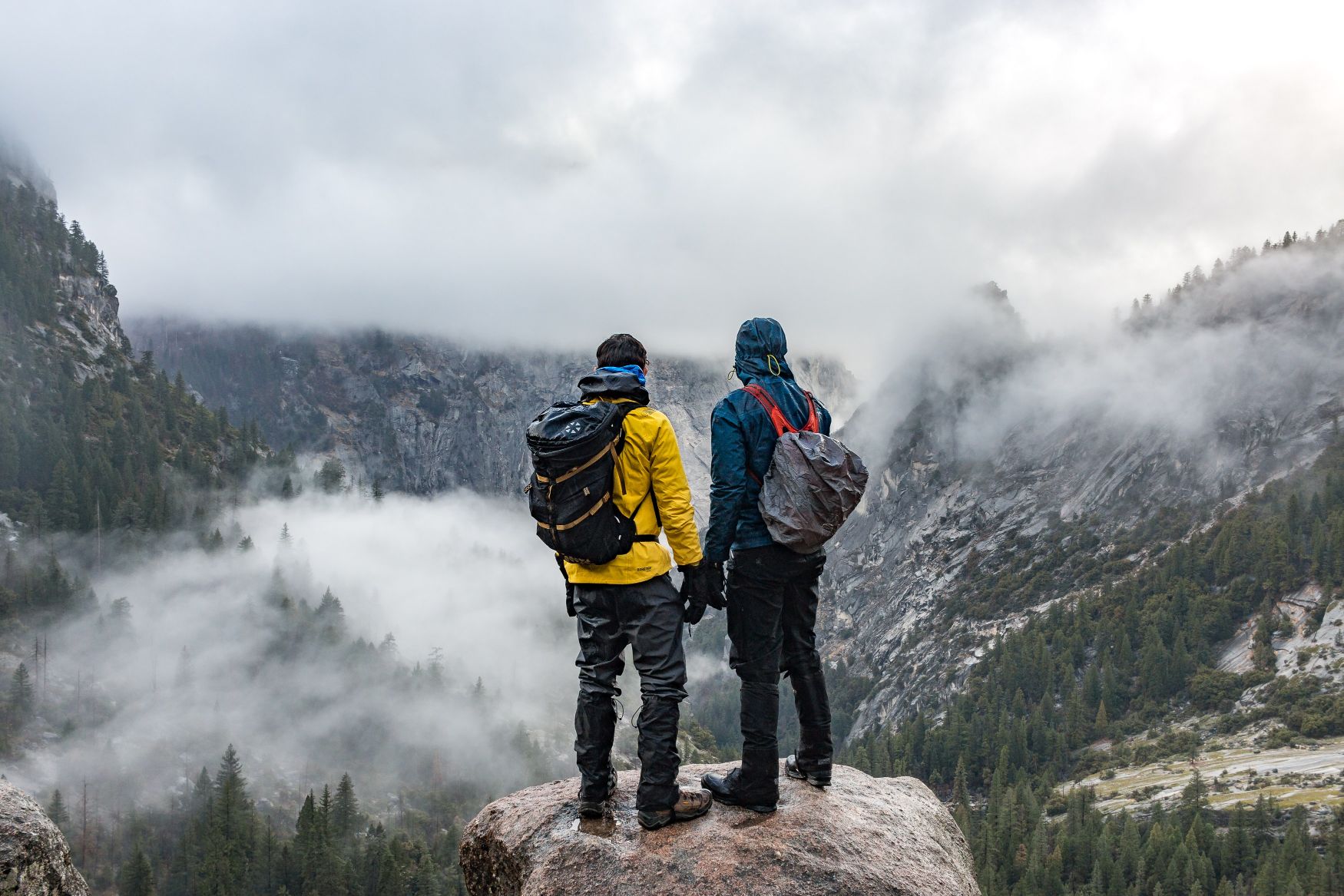 Two hikers at a viewpoint in Yosemite national park, on a cloudy day.