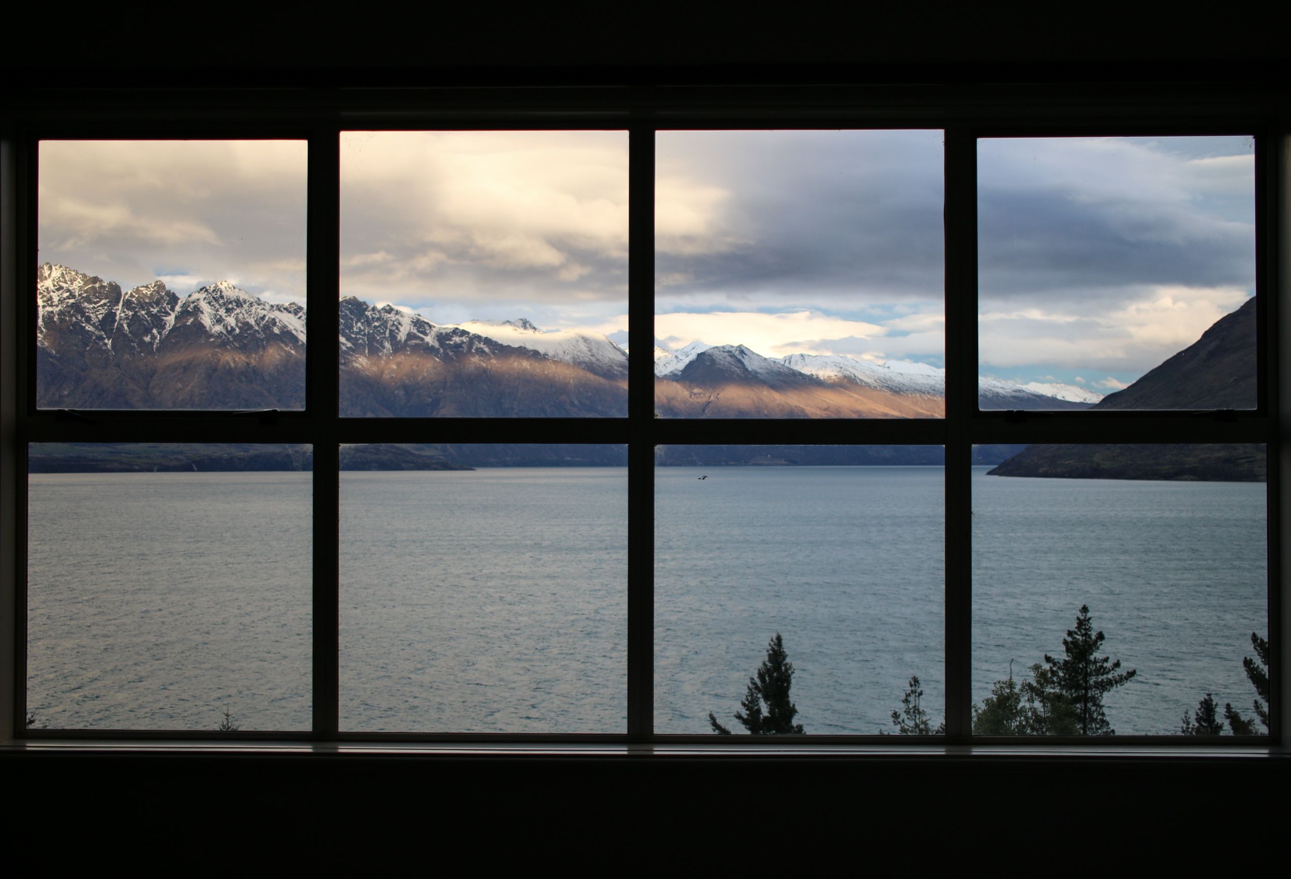 A view of snowy mountains and a lake taken through a window.