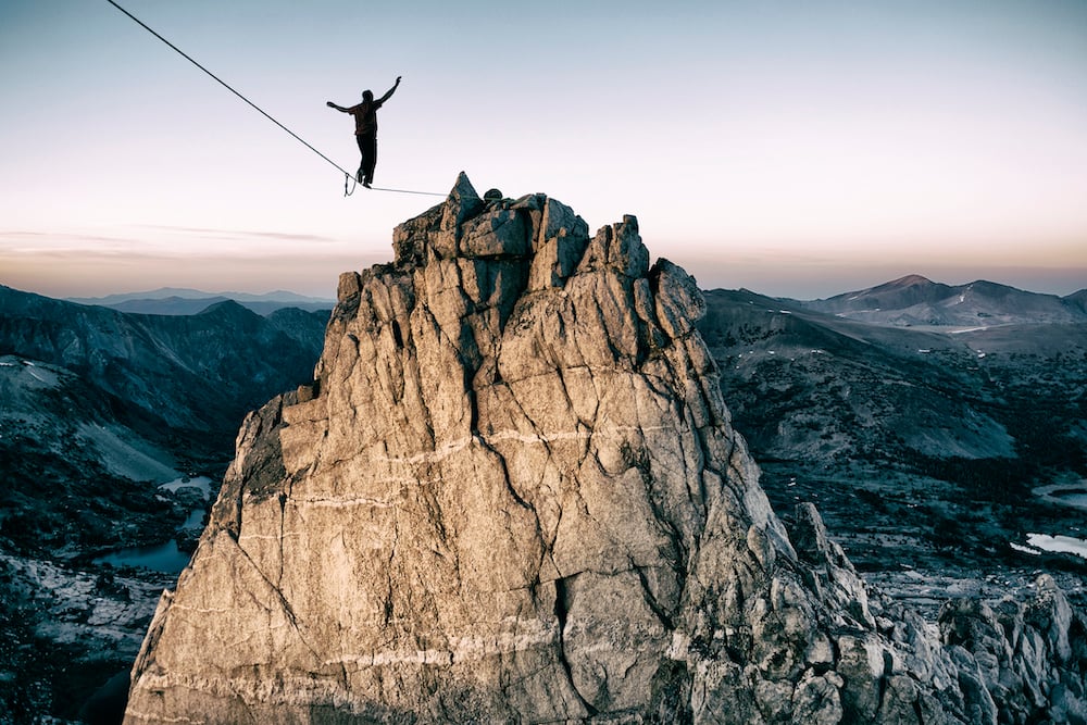 A figure crossing over to a mountain summit on a high wire