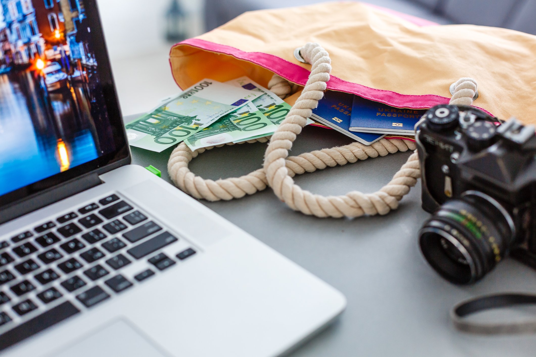Close up of a laptop, a camera, and a bag with money and passports inside.