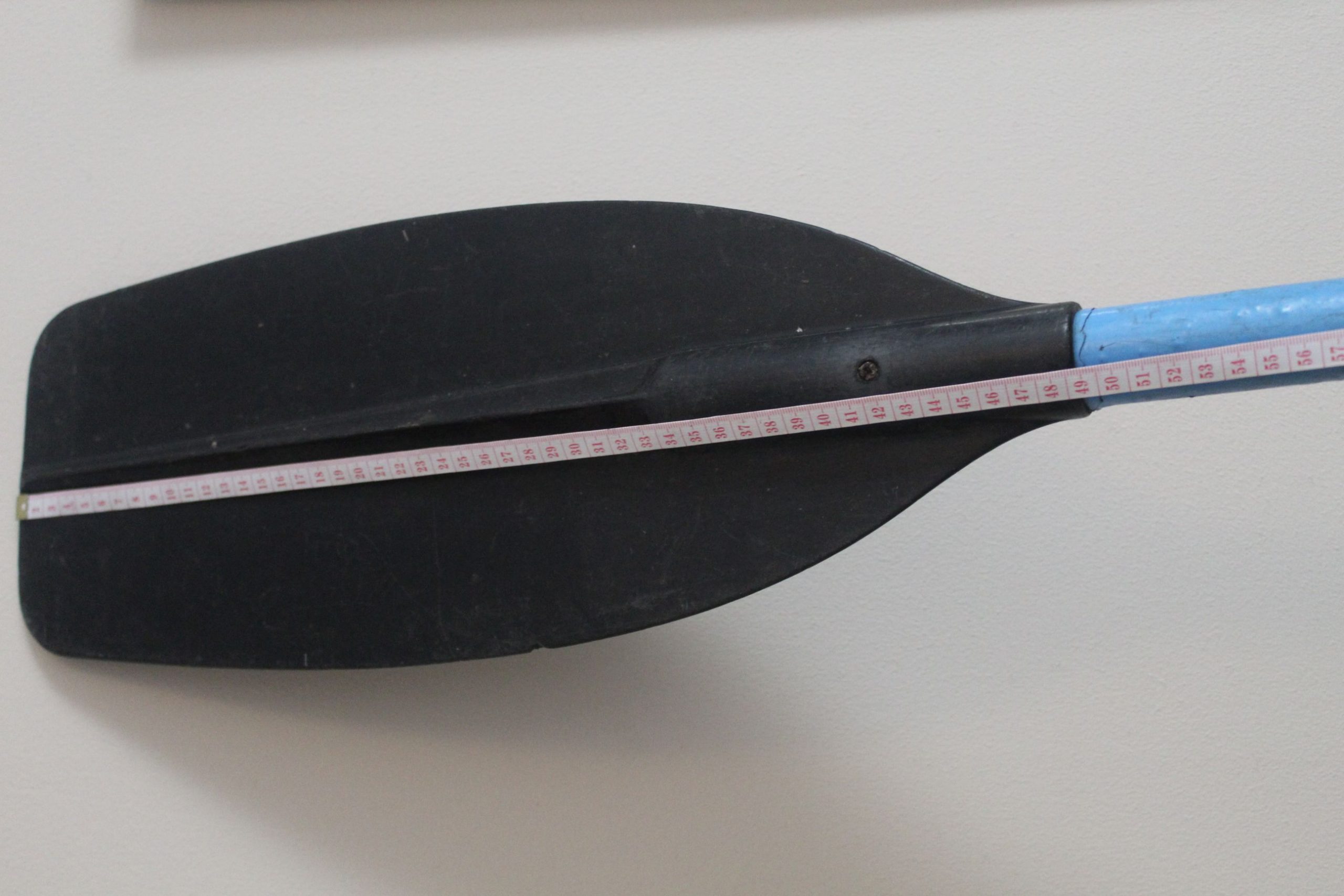 A close up of a kayak paddle with a measuring tape across it.