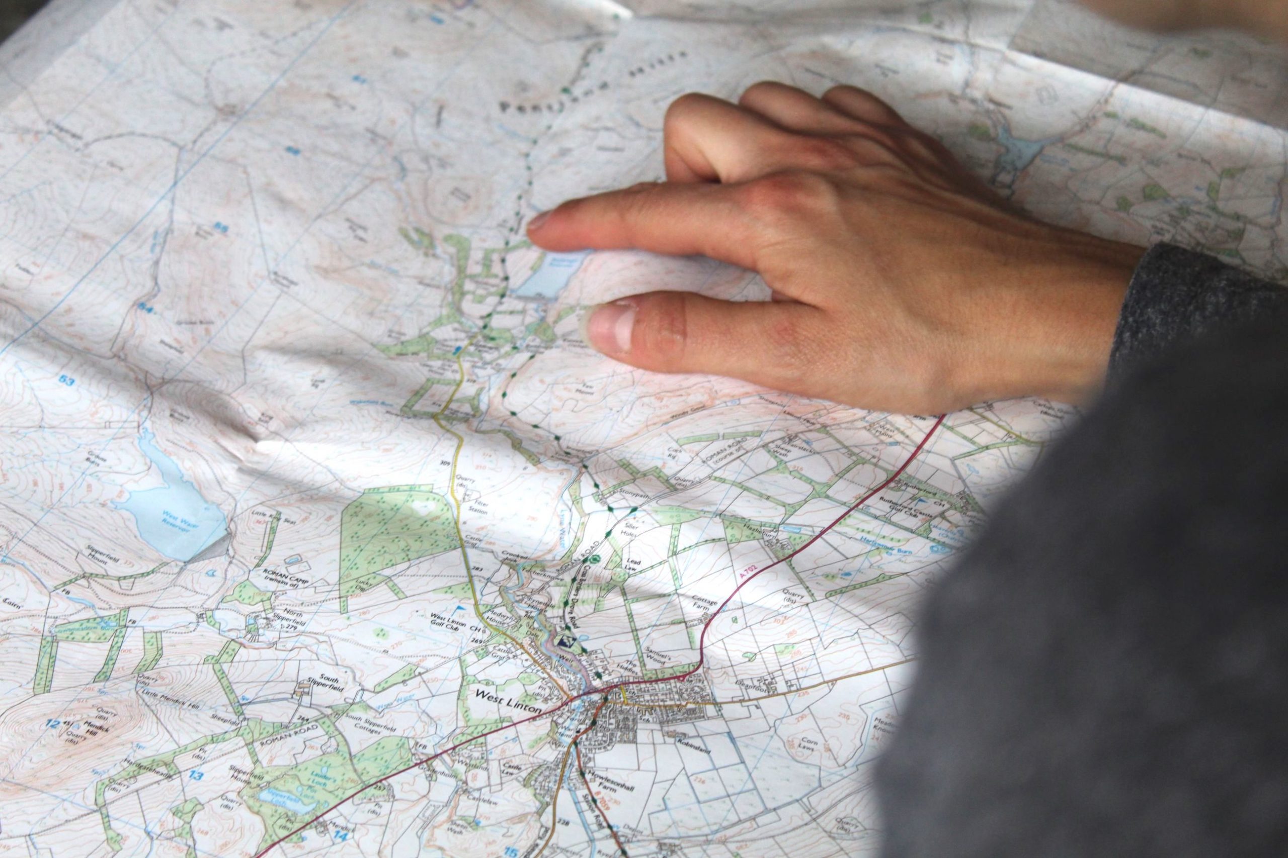 A hand hovers over an OS map of the Pentland Hills, Edinburgh, plotting a route.