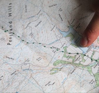 A finger points out a spot on an OS map of Edinburgh's Pentland Hills.