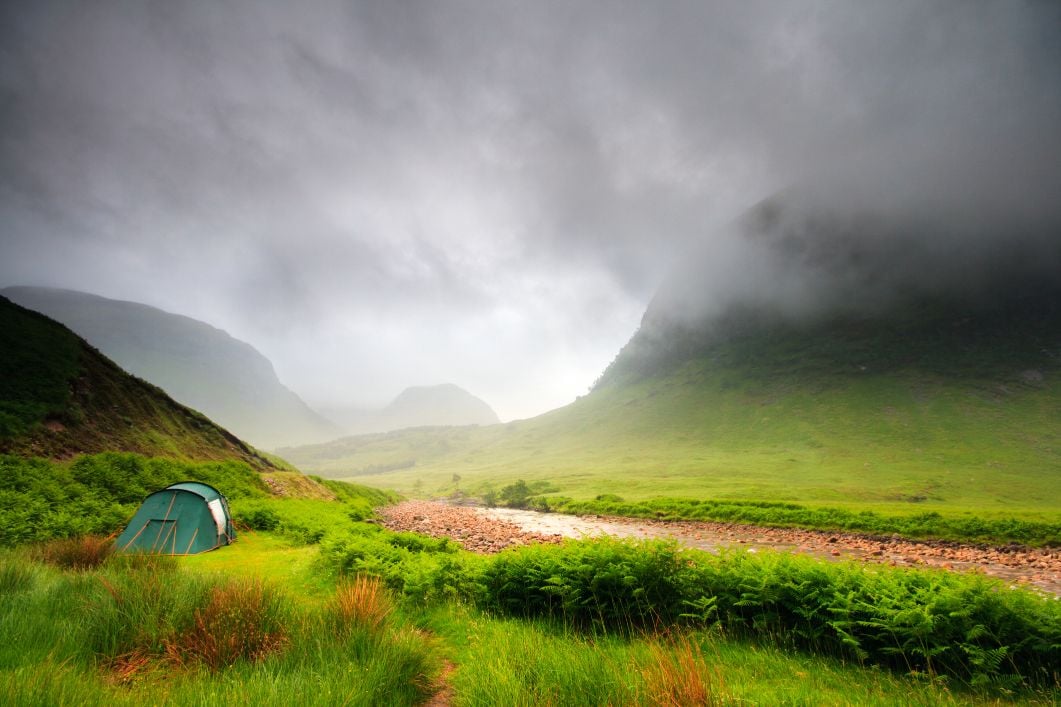 A tent is pitched on a patch of green grass in a scenic valley