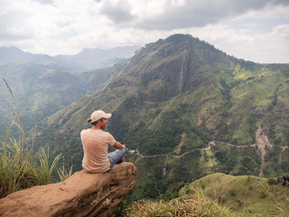 A tourist sitting on a rock looking at mountains in Sri Lanka