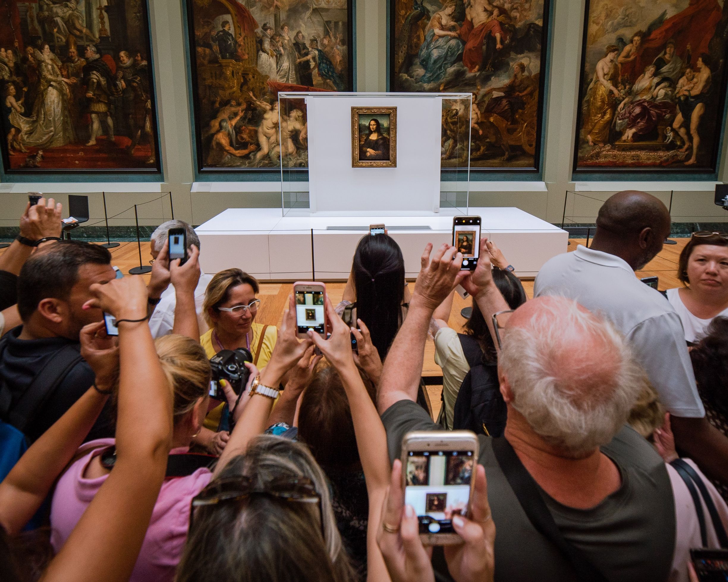 A crowd of tourists, taking photos of the Mona Lisa in the Louvre.