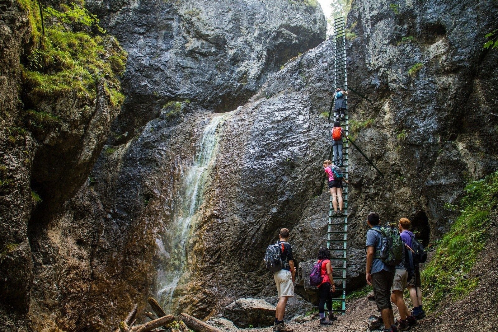 Hikers climbing a steel ladder against a cliff face in Slovakia.