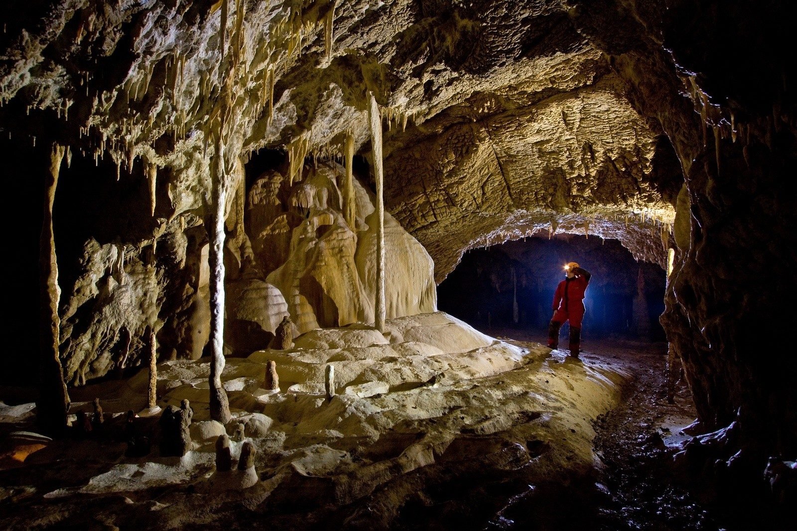 Hiker with head lamp stands in the mouth of a cave in Romania.