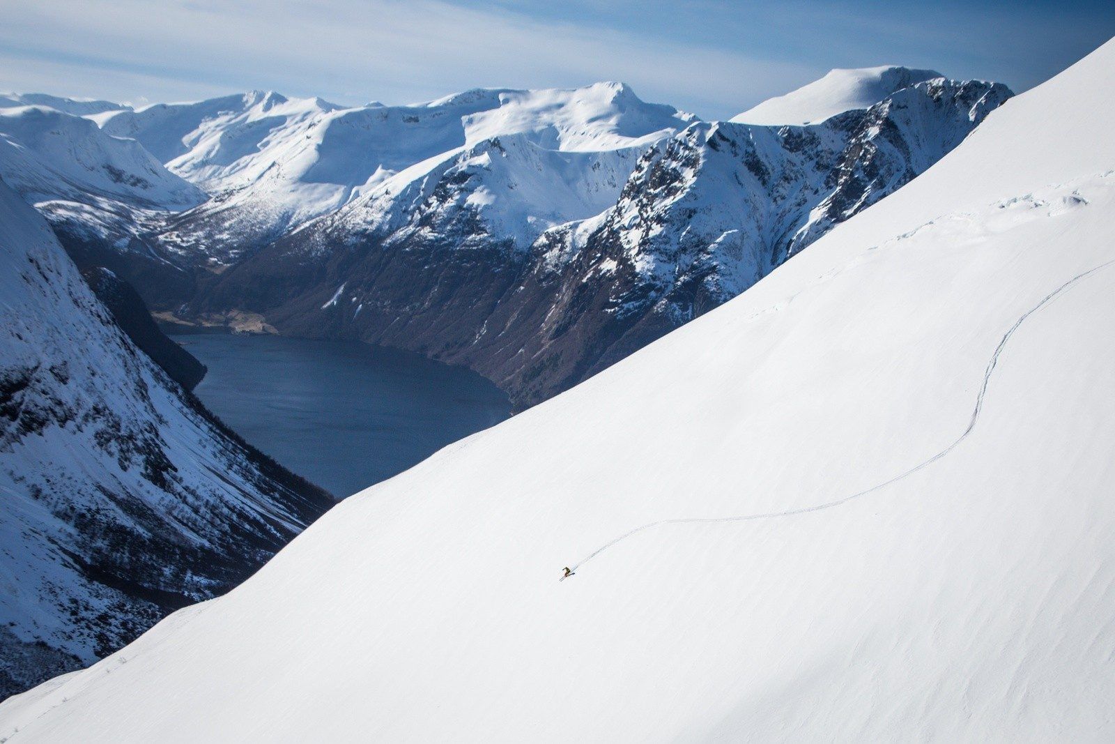 A person skis down a steep slope, making tracks in freshly fallen snow.