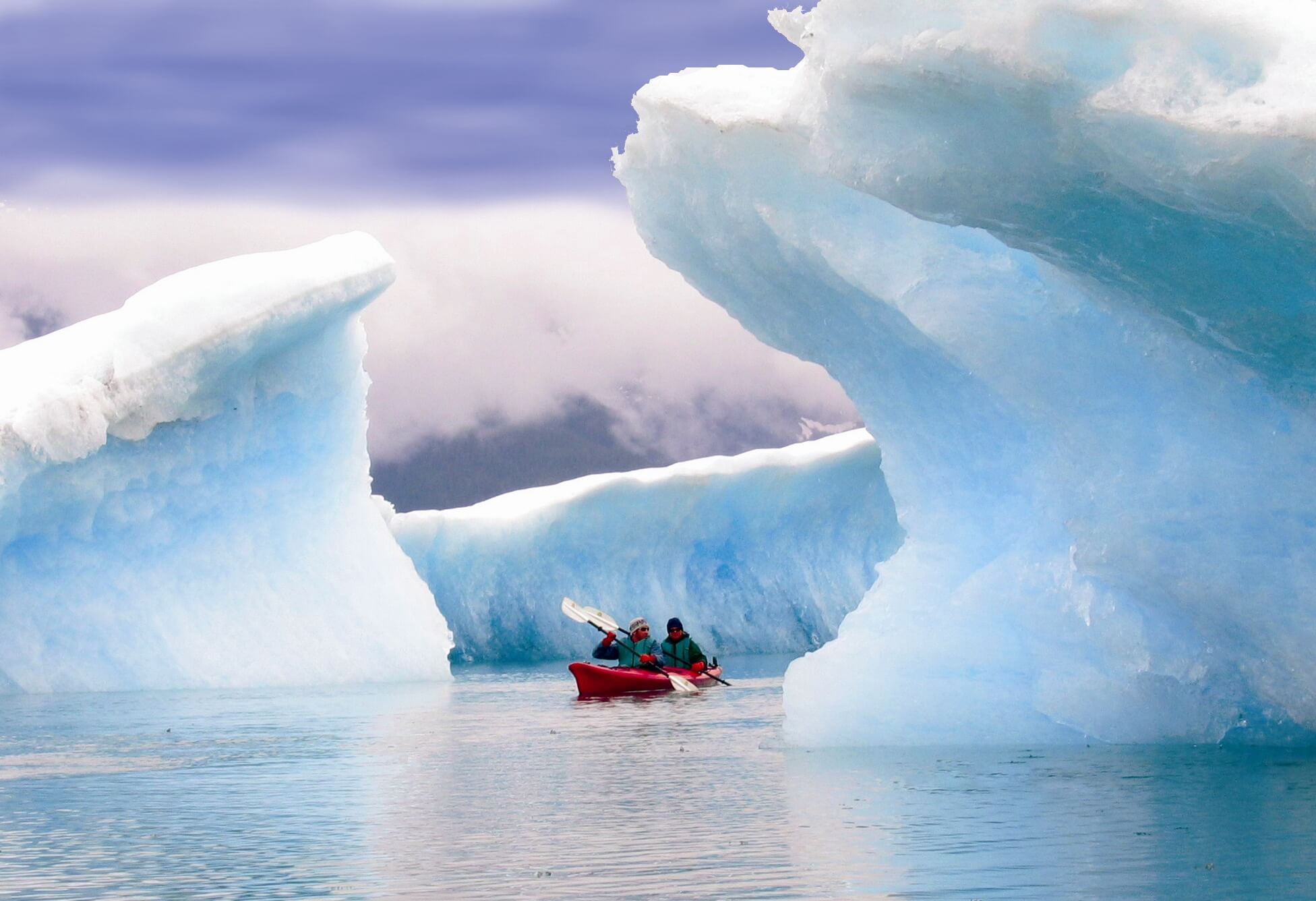 Two men kayaking on an expedition in Alaska, amongst two huge icebergs.