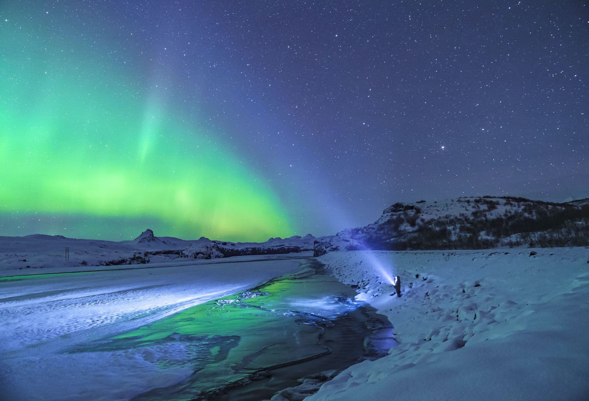 A figure stares out at a green aurora borealis in an icy landscape.