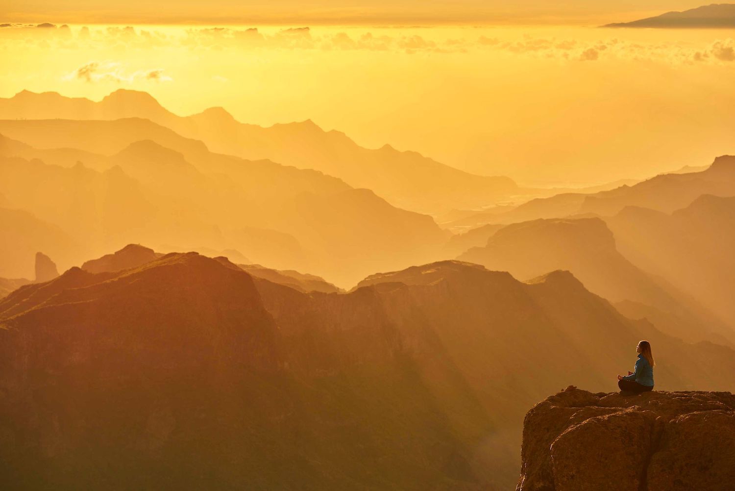 The sun sets over a national park in America, while a woman meditates on a rock.