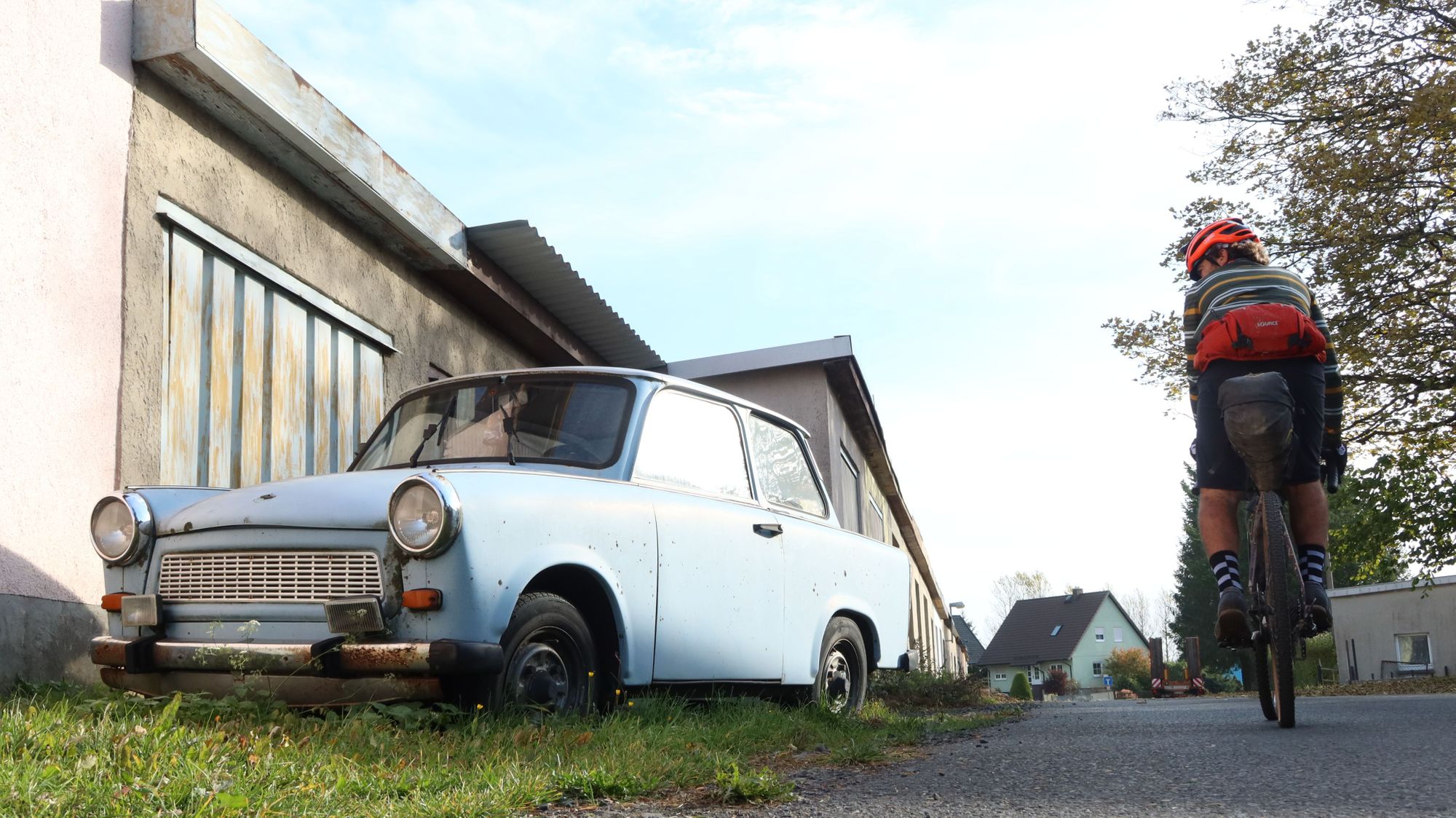 A cyclist passing a vintage car and the old Berlin Wall
