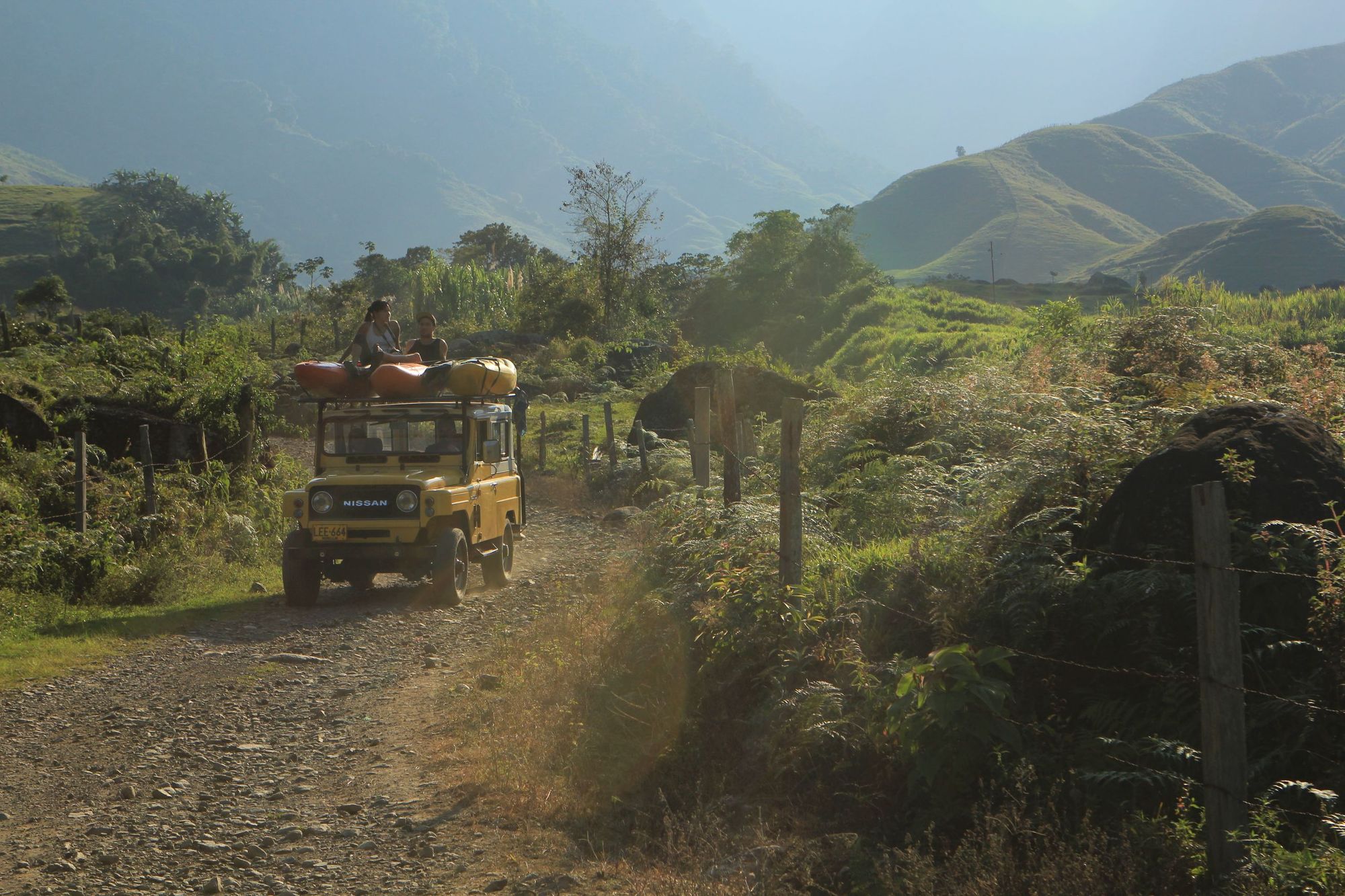 A Nissan van with two kayaks on top, and people sitting on them, driving down a track in Colombia's Samana Watershed