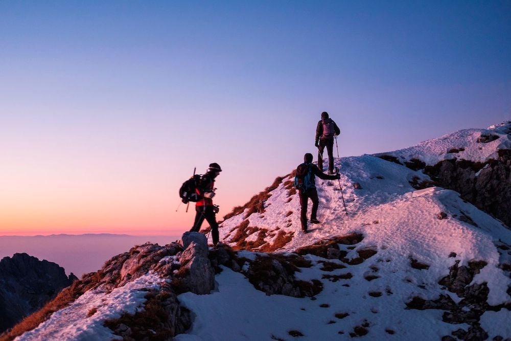 Three hikers make their way up a snowy mountain.