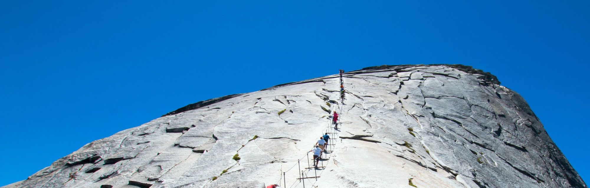 Hikers making their way to the slippery summit of Half Dome, Yosemite, along a system of cables.
