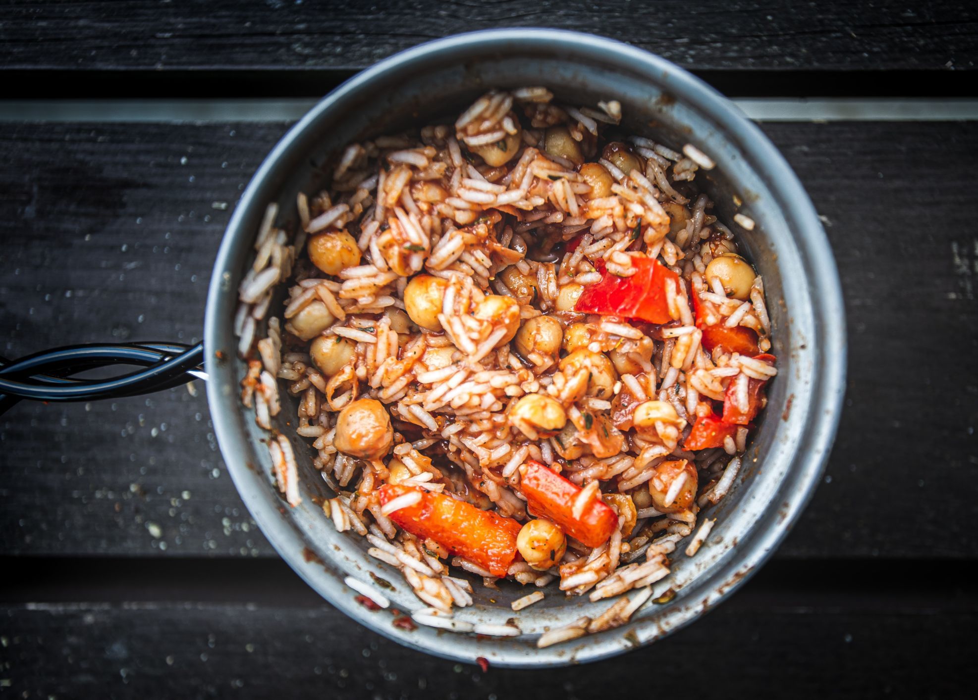 A pot of rice, nuts and carrots, served in a camping pan and placed on a picnic table.