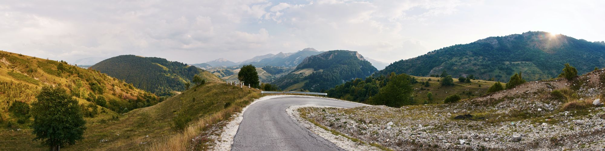 A curving road in Umoljani, Bosnia, backdropped by mountains.