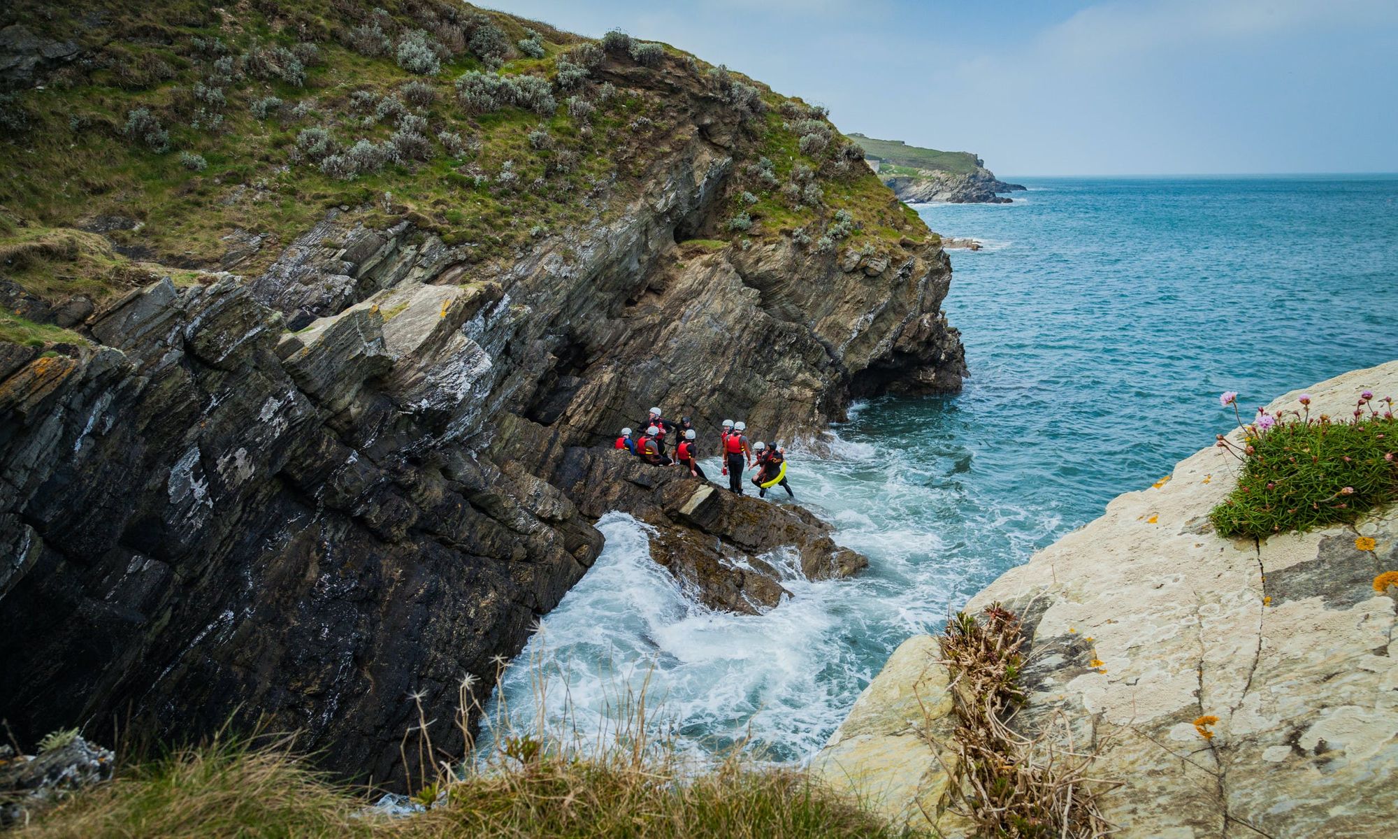 A coasteering group in Cornwall gathered on rugged rocks, down by the ocean.
