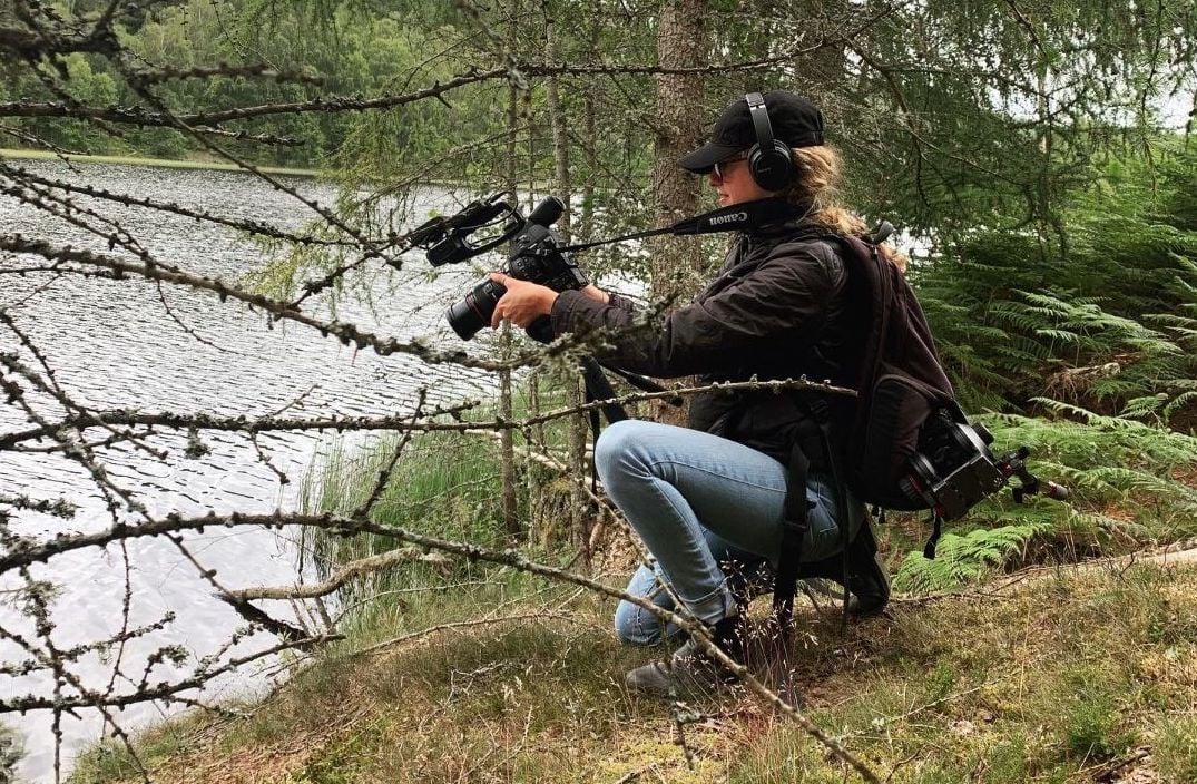 Filmmaker Nina Constable crouching by a river, filming material for 'Beavers Without Borders'