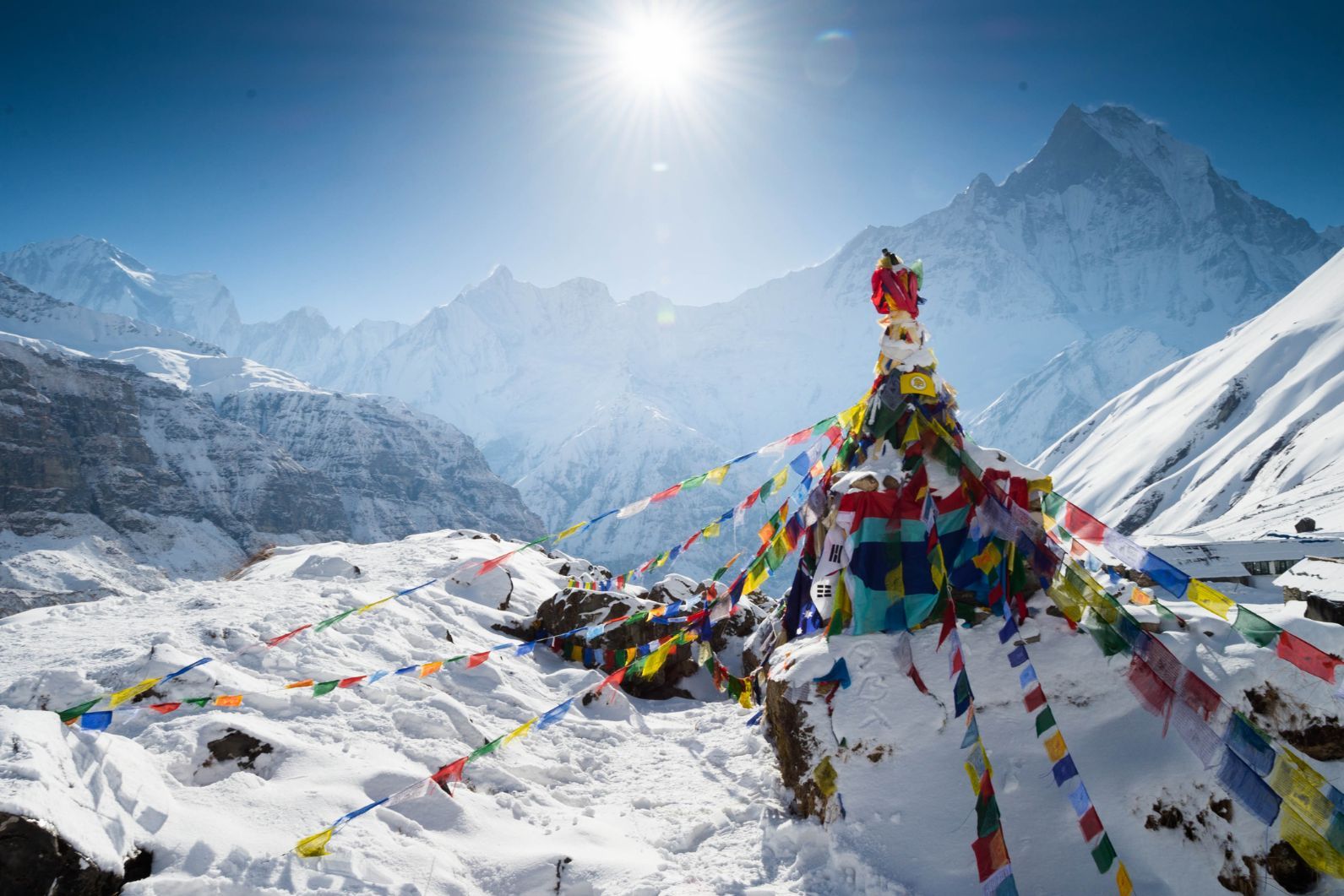A stunning, snowy high-altitude view from Annapurna Base Camp, with prayer flags in the foreground.