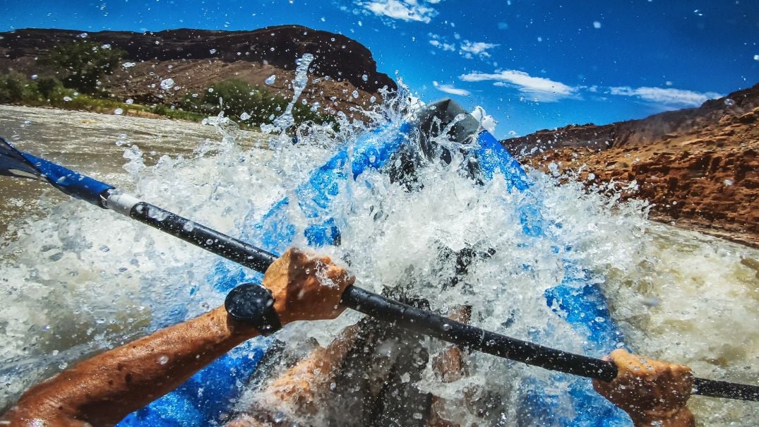 A close up of a sea kayaker's hand and paddle, in white water.